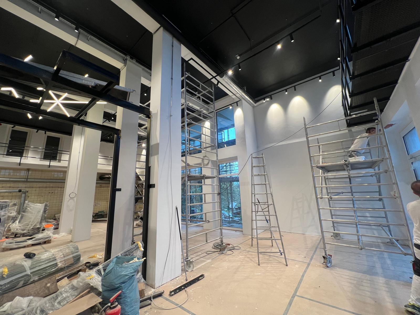 Physio Zentrum Menden – Malerarbeiten an hohen Wänden mit Gerüst, schwarze Decke und Designer-LED-Leuchten
