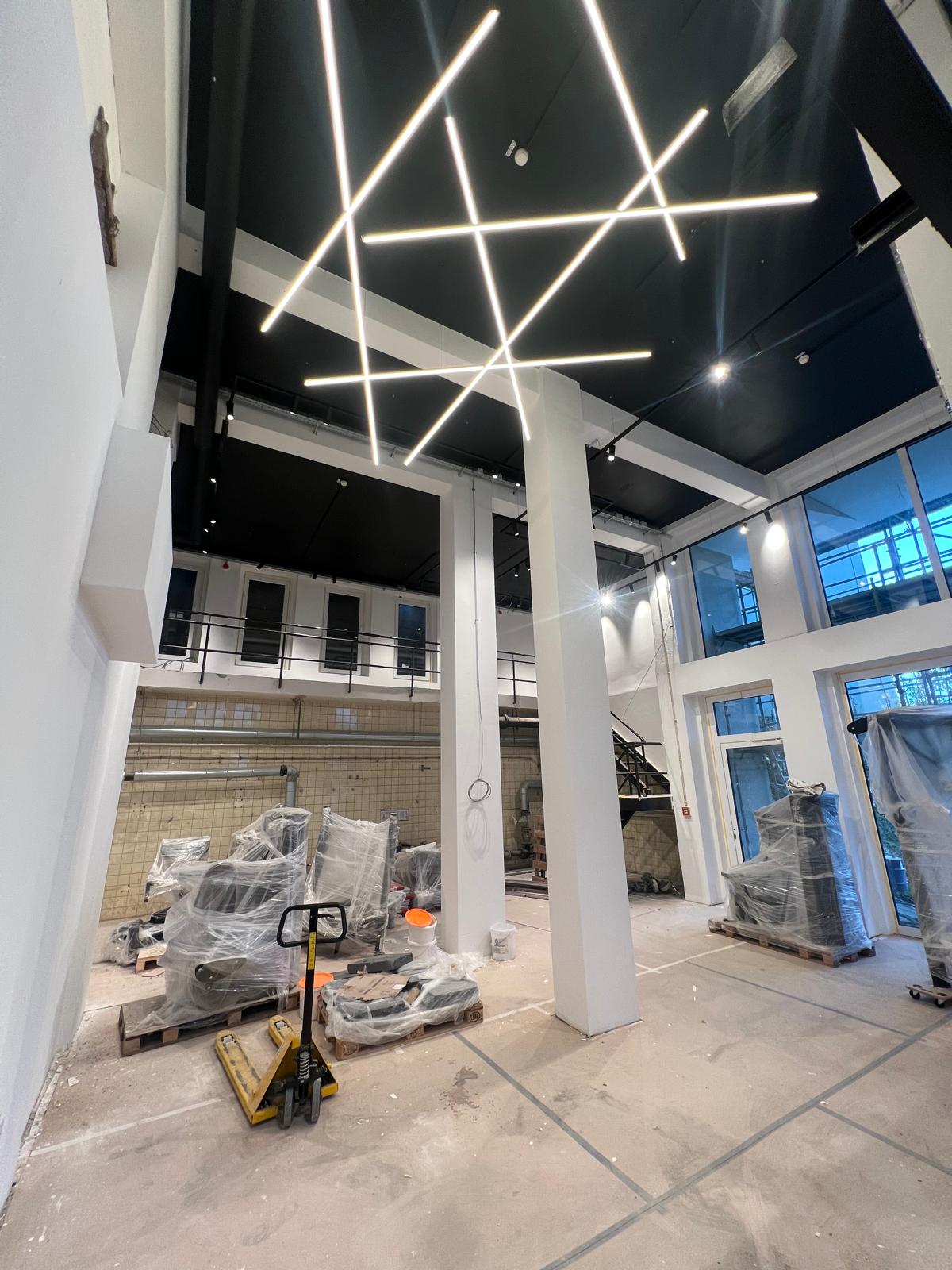 Physio Zentrum Menden – Hohe Halle mit kreuzförmigen LED-Lichtbändern an schwarzer Decke