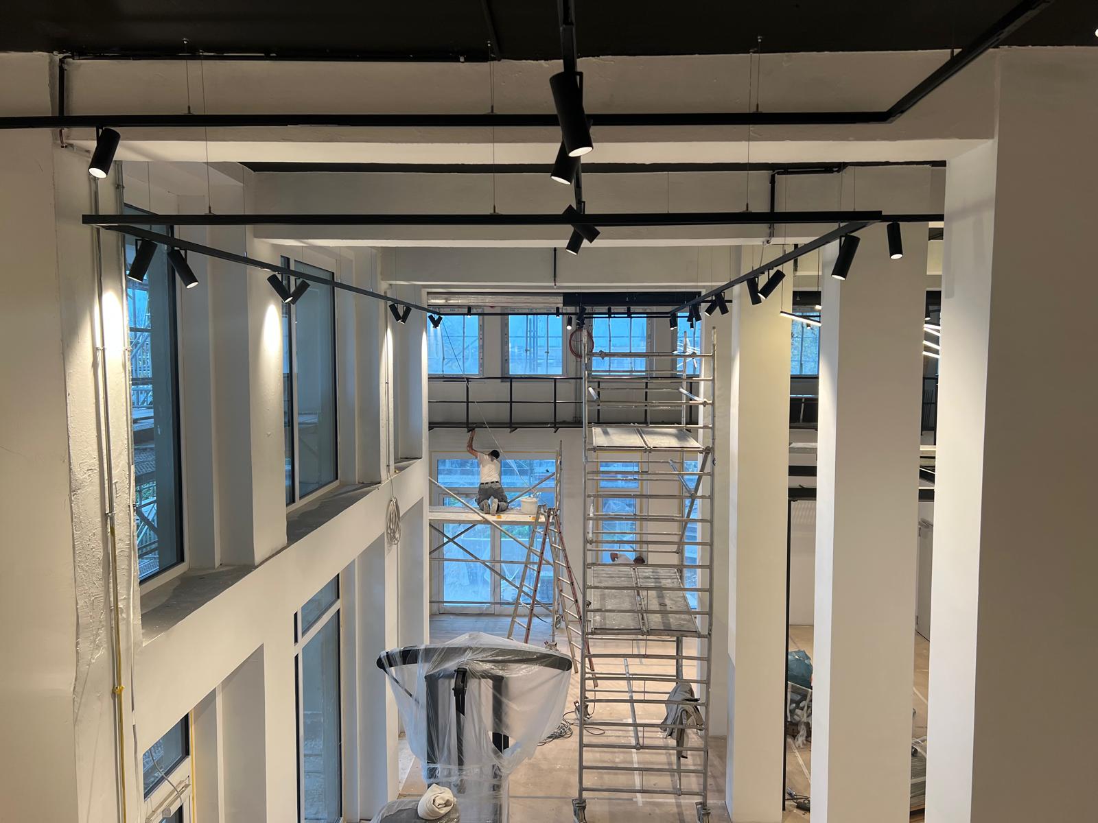 Physio Zentrum Menden – Arbeiter auf Gerüst bei Malerarbeiten, Spotlights an schwarzen Schienen