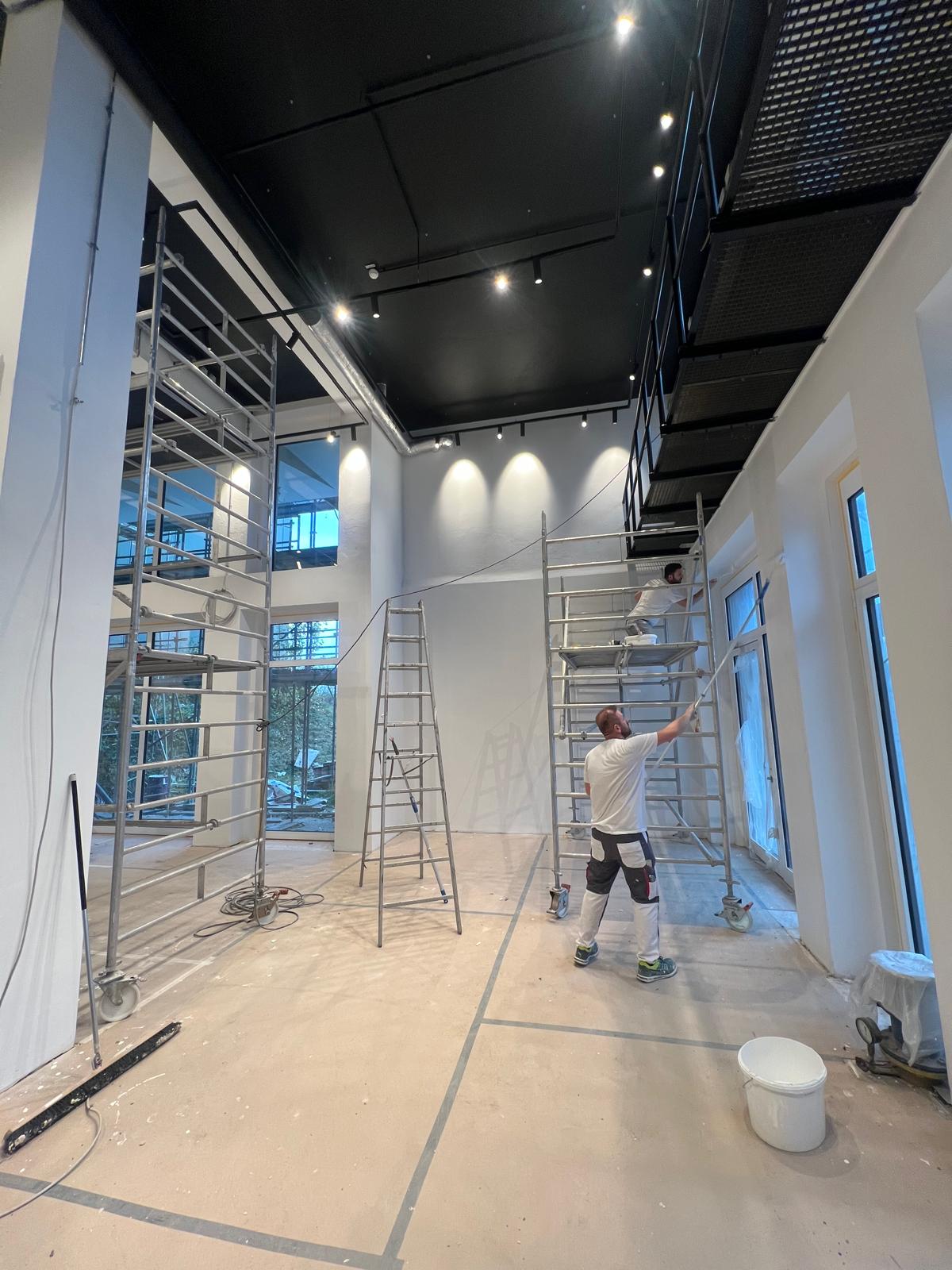 Physio Zentrum Menden – Malerarbeiten mit Gerüst in hoher Halle, schwarze Rasterdecke mit Spots